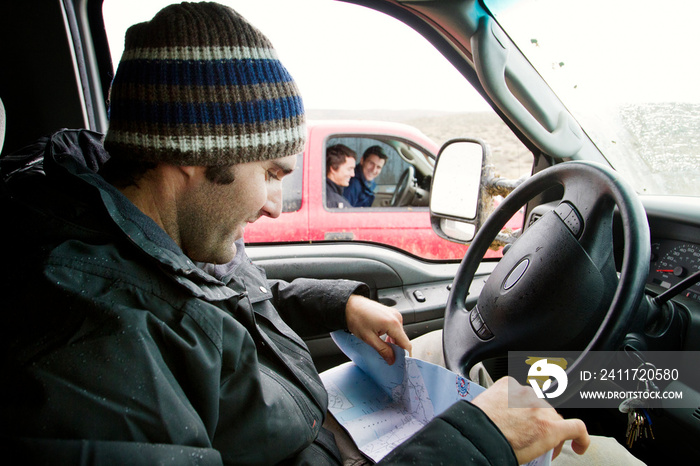 Man reading map while traveling in car with friends in background during winter