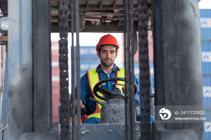 Male container yard worker driving and operating on diesel container forklift truck at container terminal. Male worker wear safety helmet, uniform and driving forklift truck at commercial dock site