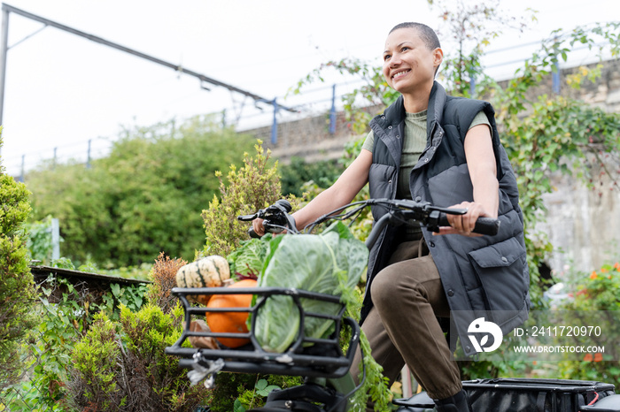 Smiling woman riding cargo electric trike loaded with homegrown vegetables