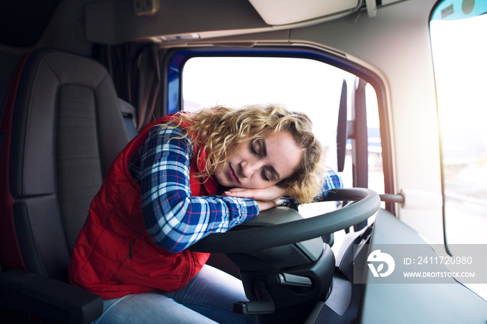 Sleepy and tired female truck driver sleeping over steering wheel inside truck vehicle cabin. People working overtime.