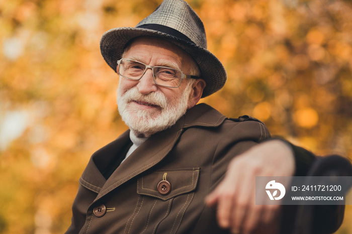 Closeup photo of funny glad old pensioner grey haired grandpa central park walk enjoy sunny day warm weather sit bench break pause wear stylish autumn jacket hat specs colorful street outside