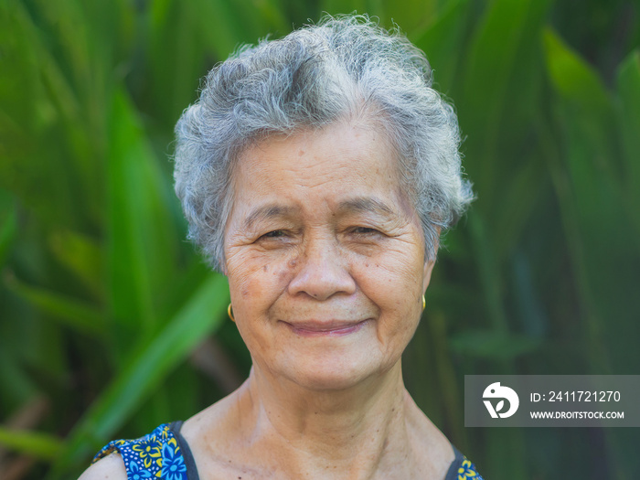 Beautiful elderly Asian woman looks at the camera with a smile while standing in the garden