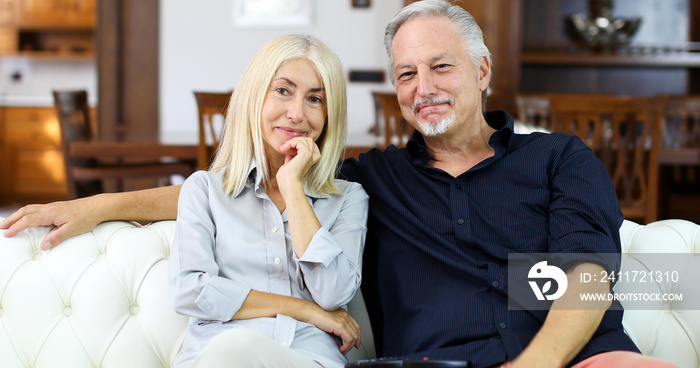 Portrait of a happy mature couple in their home watching tv together