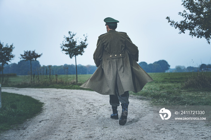 Rear view of vintage 1940s military officer walking on rural roa