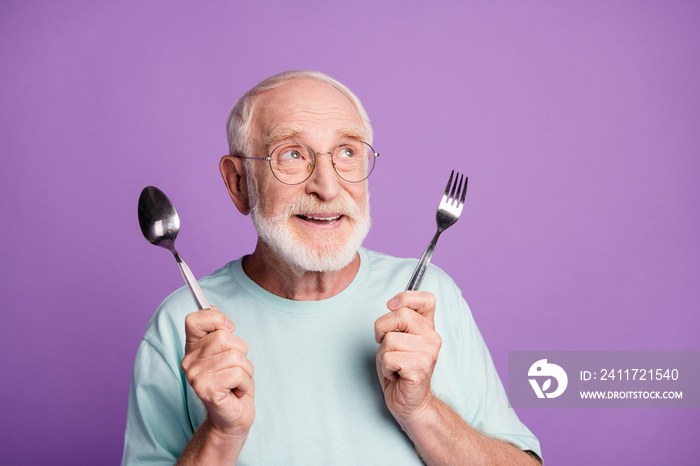 Portrait of funny smiling grandfather hold cutlery looking empty space wear light blue t-shirt isolated over violet color background