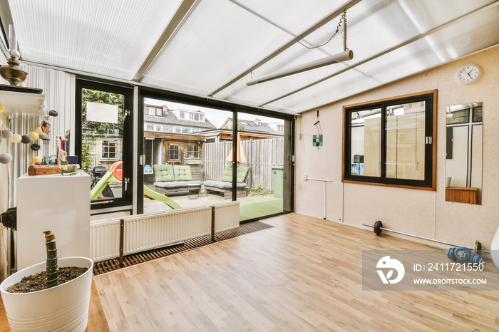 Spacious bright room with wooden floor, radiator, dumbbells, barbell and windows and door to the yard