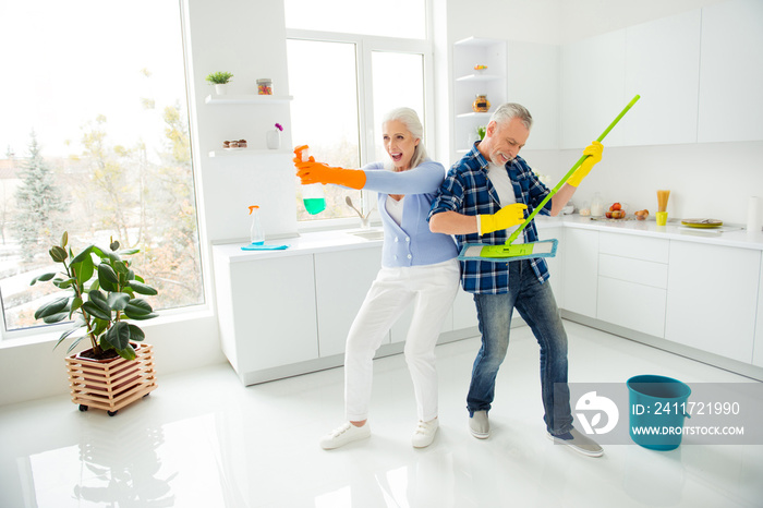 Full size, fullbody portrait of crazy foolish funny mad cool couple of senior ready to fight with dust, man playing on mop like guitar, woman holding spray like gun and ready for shooting