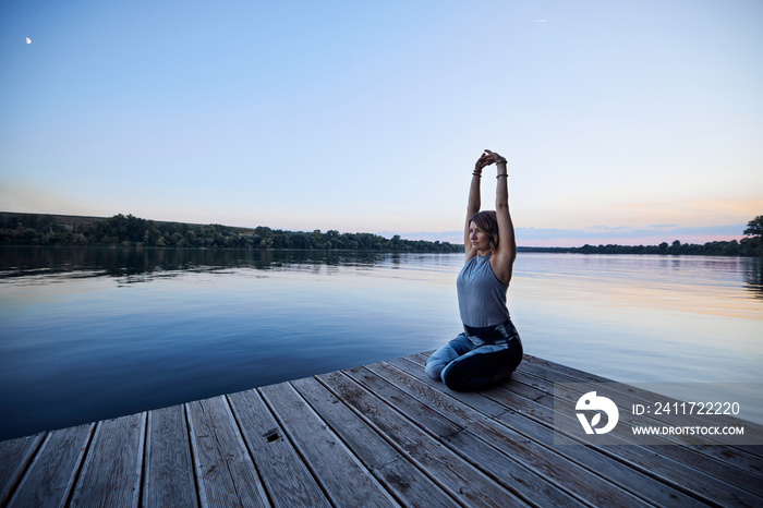A calm yogi woman in a practices yoga on a dock.
