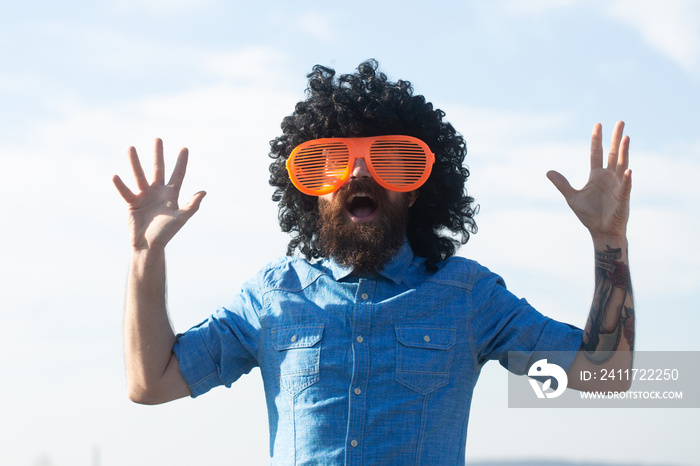 Crazy funny bearded man with wig and fun glasses on sky background. Funny facial expressions.