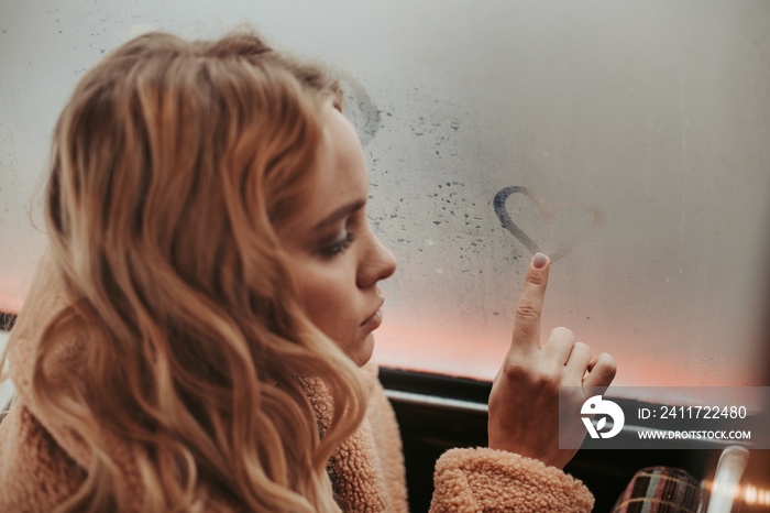 Dreamful lady drawing heart shape on window