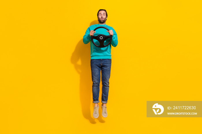 Full length photo of cheerful positive guy dressed teal outfit jumping high riding auto isolated yellow color background