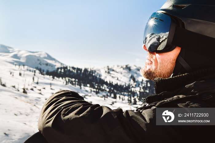 Close up of the ski goggles of caucasian man with the reflection of snowed mountains and sunburst. A mountain range reflected in the ski mask. Portrait of man at the ski resort