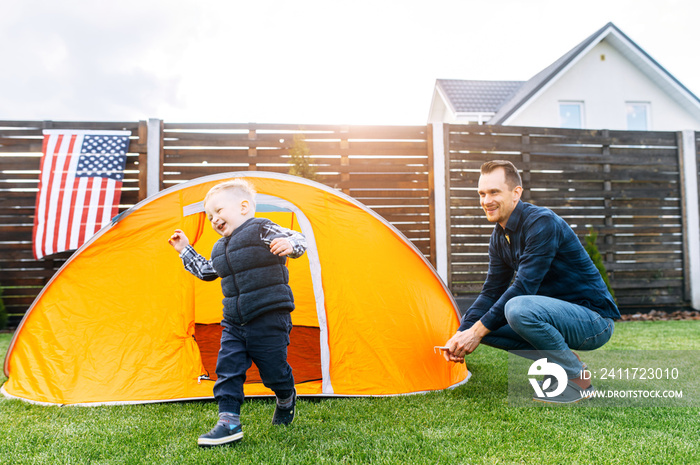 Father and son have wonderful day together. Young father and his cute toddler boy camped in the backyard, they are playing in a tent