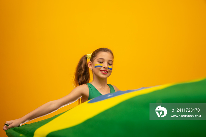 Football supporter, Brazil team. World Cup. Beautiful little girl cheering for her team on yellow background
