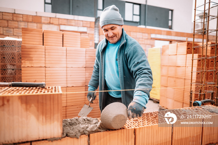 industrial details - Construction bricklayer worker smiling and building walls with bricks, mortar and rubber hammer