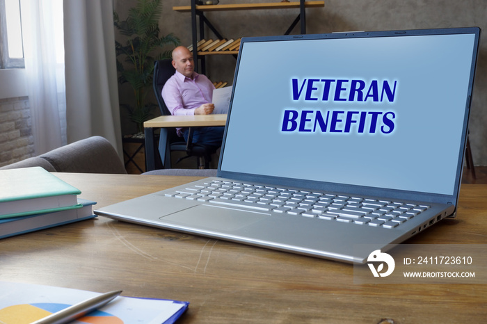 Financial concept meaning VETERAN BENEFITS with phrase on the Compact laptop A successful businessman with documents on the background