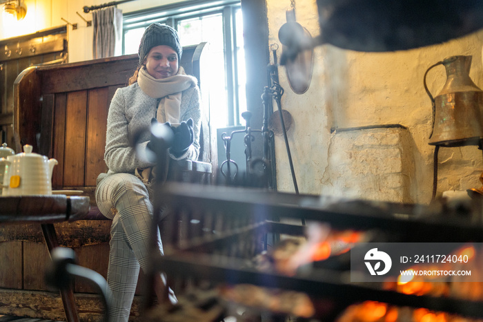 Young beautiful woman warming up with tea by fireplace