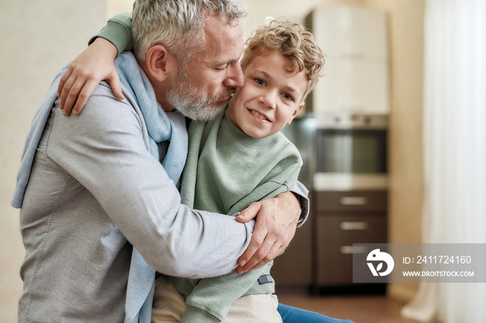 Hug time. Happy grandfather embracing his cute little preschool grandson while standing together at home