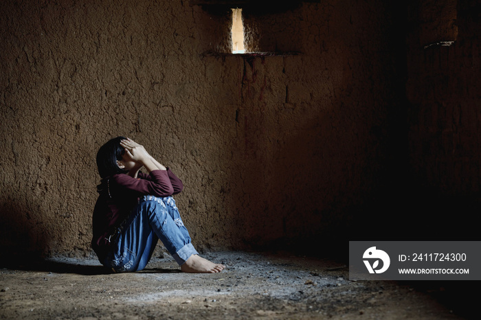 Sad and depressed little girl sitting in an old empty room. Human trafficking concept.