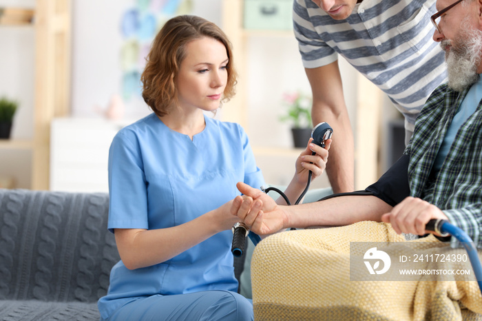 Young caregiver measuring blood pressure of senior man at home