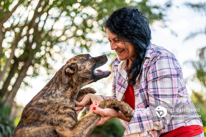 Portrait of smiling beautiful female farmer with a dog. Woman at farm in summer day. Gardening activity. Brazilian elderly woman. Latino people.
