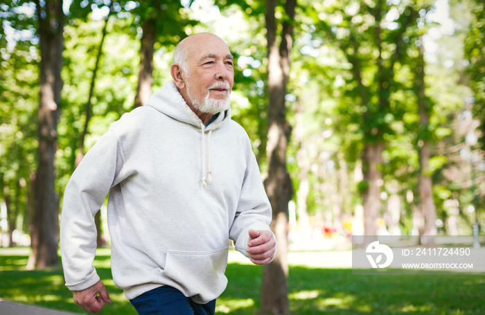 Elderly man running in green park, copy space