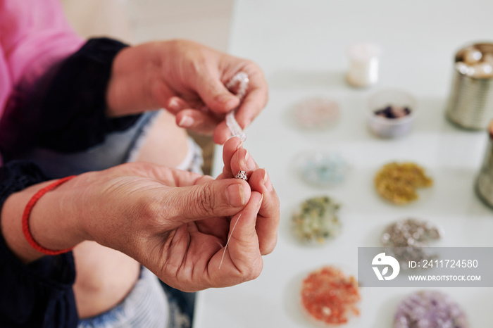 Hands of woman putting crimp bead on string with semi-precious stones to complete the bracelet or necklace