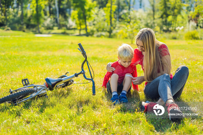 The boy fell off the bicycle, his mother pastes a plaster on his knee