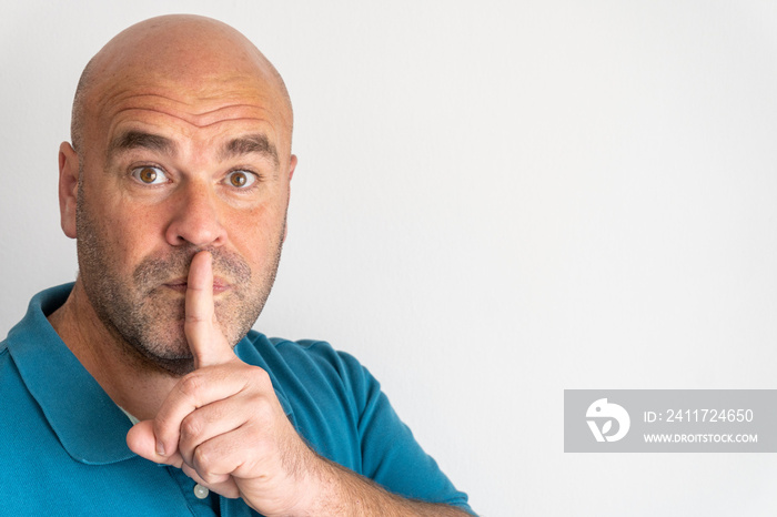 Portrait of middle aged Caucasian man asking for silence with a finger covering his mouth, on white background.