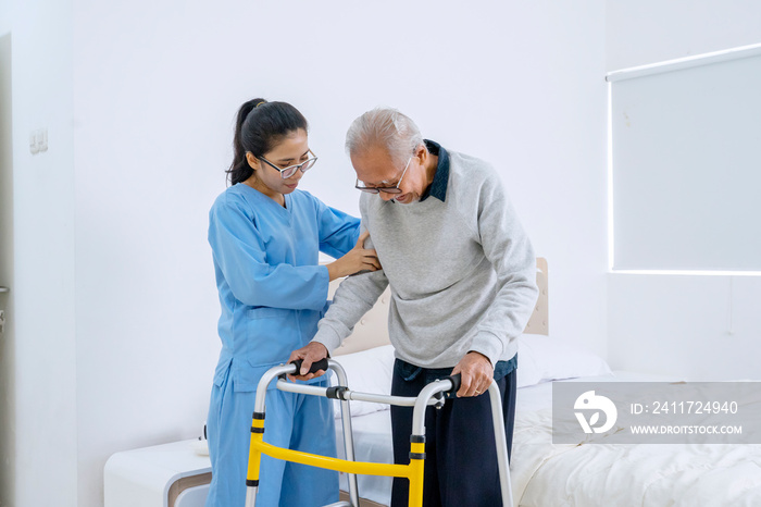 Beautiful nurse helping old man to walk in bedroom