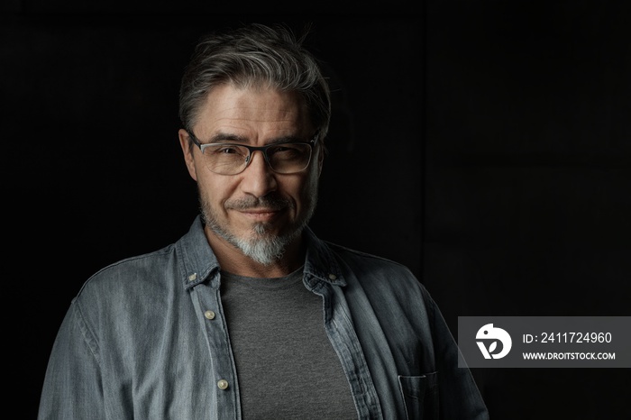 Portrait of casual older man with beard against dark background.