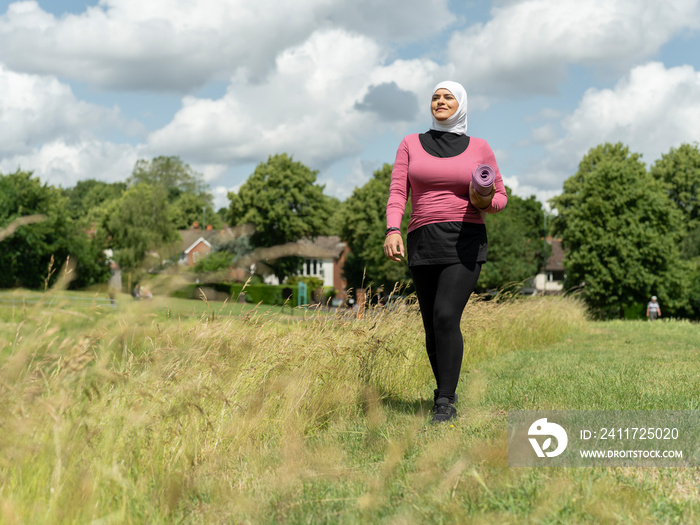 UK,Sutton,Woman in headscarf carrying yoga mat in meadow