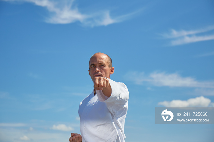 Adult athlete training hand kick against blue sky