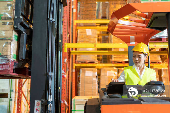 Forklift driver asian young woman in safety jumpsuit uniform with yellow hardhat at warehouse. Worker female  working and control in forklift loader work