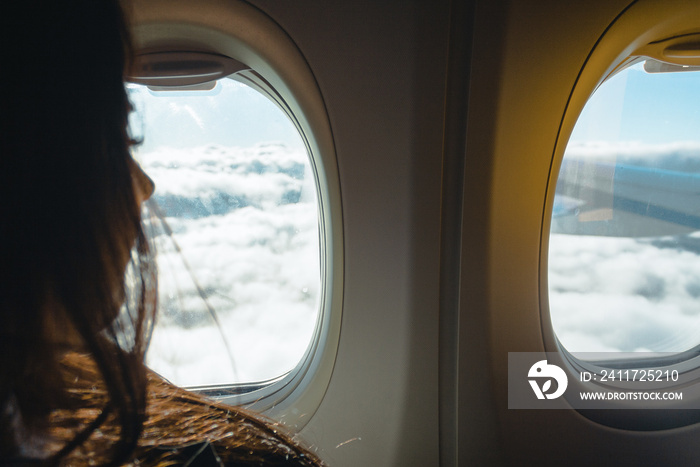 Young woman looking into window in a plane. Woman in a plane. Woman looking into porthole. Traveling by plane concept. Air travelling.