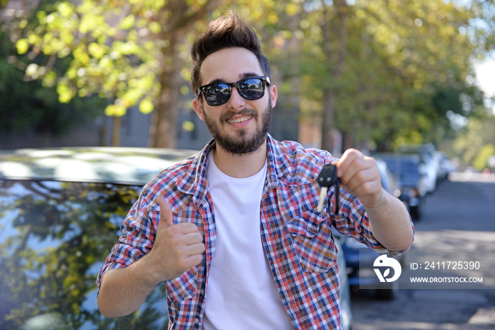 Successful young man with key standing near car