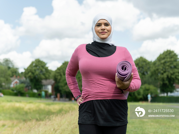 UK,Sutton,Portrait of woman in headscarf standing in meadow with yoga mat