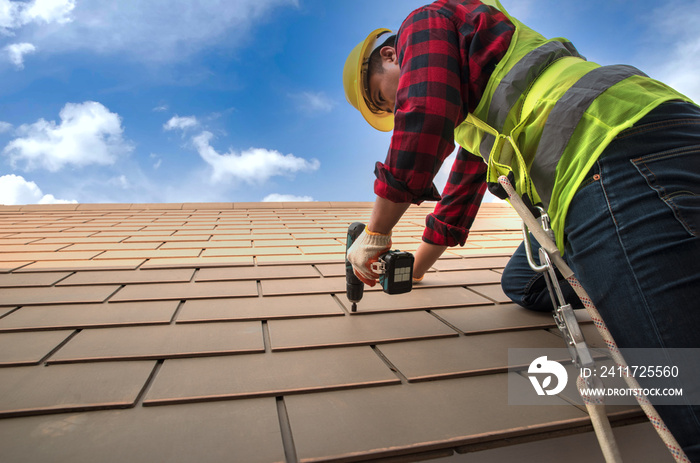 Construction roof repair workers in protective clothing safety in fashion jeans shirt Wear gloves, use a drill, repair and replace roof with blue sky background and goppy space.