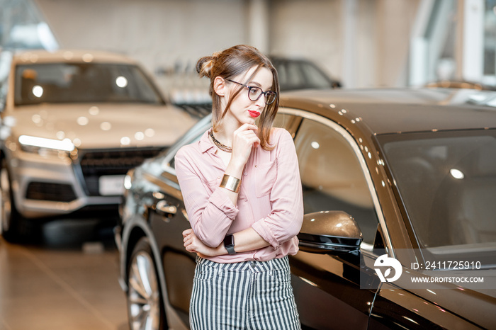 Young beautiful woman hesitates choosing a new car in the showroom