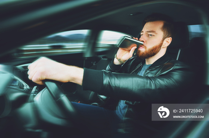 A drunken man driving a car with a bottle of alcohol in his hand. Man whiskey from an iron flask behind the wheel of a car