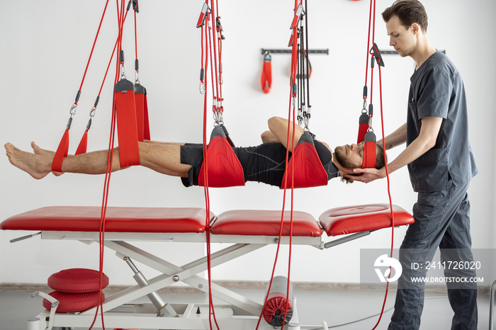 Rehabilitation specialist doing active treatment on suspension straps to a male patient. Concept of therapeutic exercises to restore pain-free movement patterns and improve function