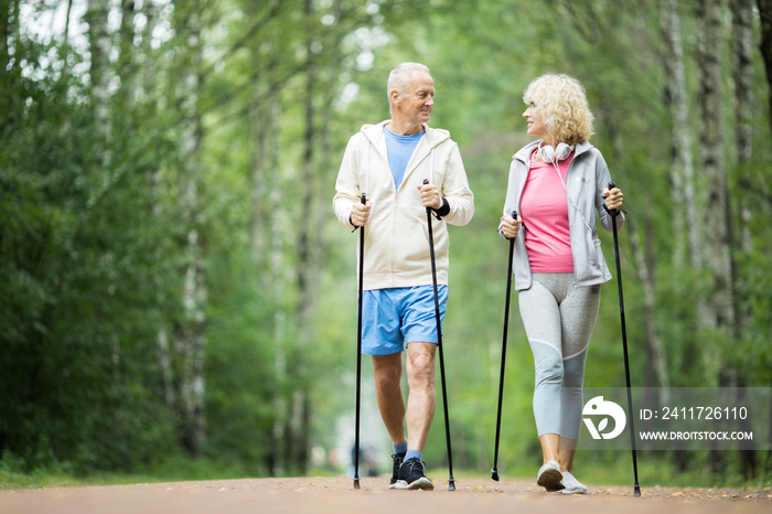 Senior active couple practicing trekking in park among green trees on summer weekend