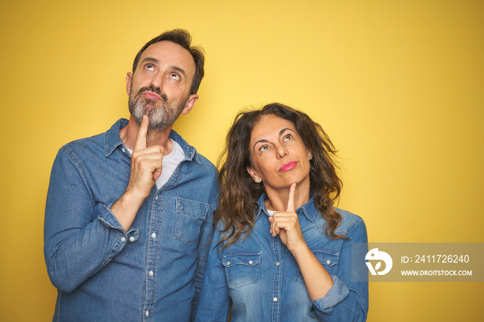 Beautiful middle age couple together standing over isolated yellow background Thinking concentrated about doubt with finger on chin and looking up wondering