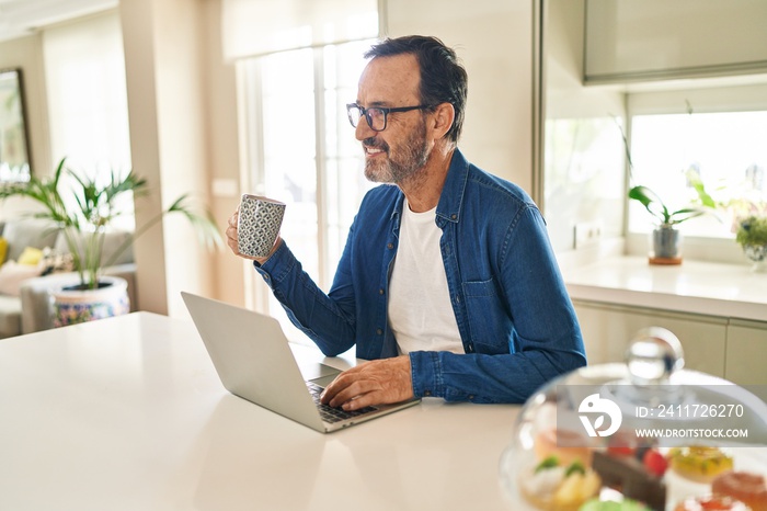 Middle age man using laptop drinking coffee at home