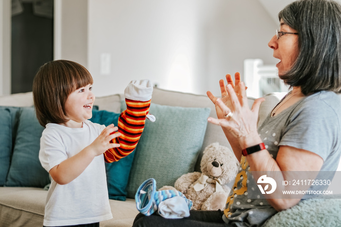 Cute little cheerful child playing with his granmother with bright hand-toy at home. Focus on boy. Family lifestyle. Active senior woman. Babysitting.