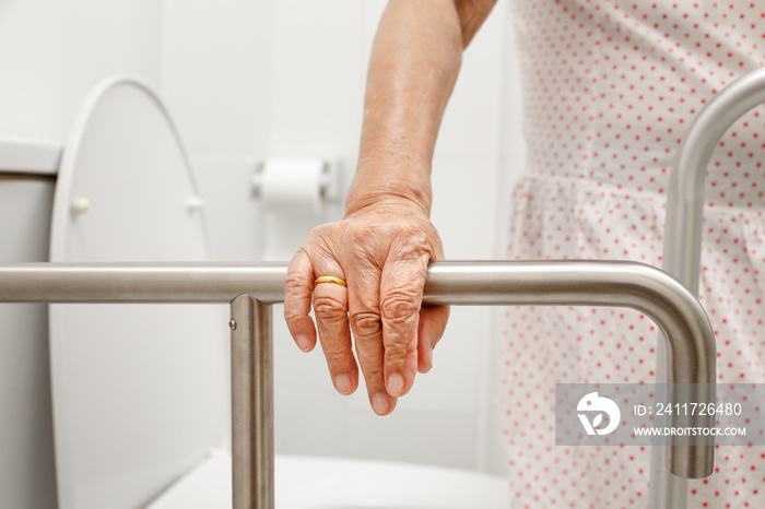 Elderly woman holding on handrail in toilet.