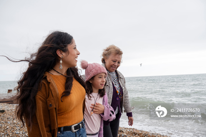 Grandmother, mother and daughter walking on beach on cloudy day