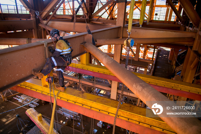 Industrial rope access rigger miner worker wearing safety harness, helmet working at height ringing anchor on tie line  abseiling inspecting 3 tone lifting sling prior to used construction site Perth