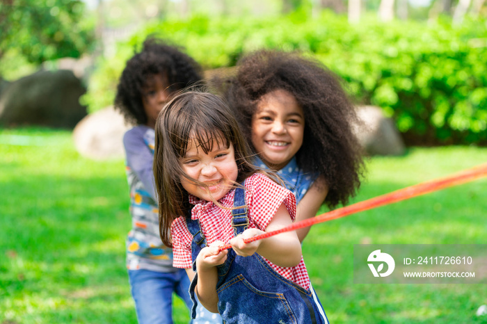 Happy children playing tug of war and having fun during summer camping in the park. Children recreation concept.