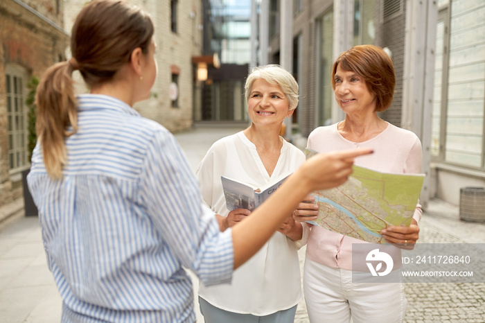 tourism, travel and friendship concept - female passerby showing direction to senior women with city guide and map on tallinn street